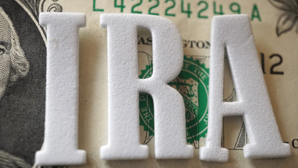 Close-up of white felt letters 'IRA' on dollar bills background.