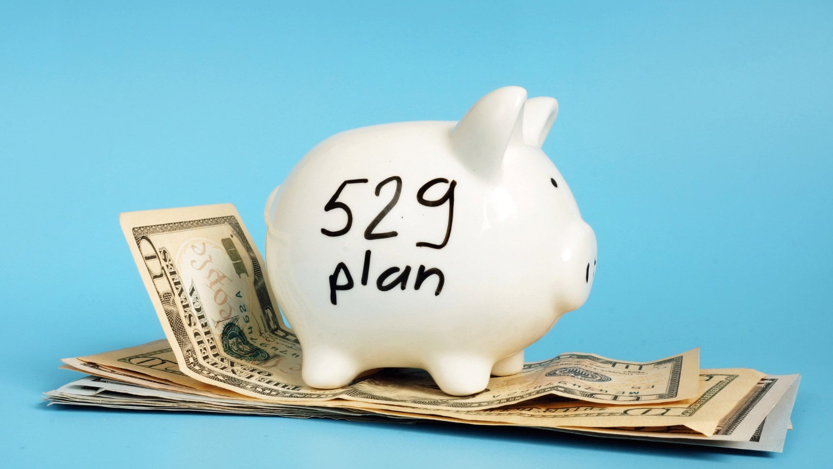 White piggy bank with '529 plan' written on it, on top of dollar bills.