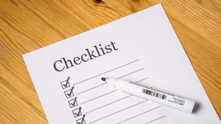 Checklist with checkmarks and pen on wooden surface for financial review.